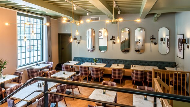 A restaurant with a modern interior, featuring a mix of wooden and upholstered seating, a variety of pendant lights, and a series of mirrors on the walls. - Boutique Hotel Rijks I Kloeg Collection (Goes)