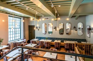 Un restaurante con una decoración moderna, que presenta una mezcla de asientos de madera y tapizados, varios candelabros colgantes y una serie de espejos en las paredes.