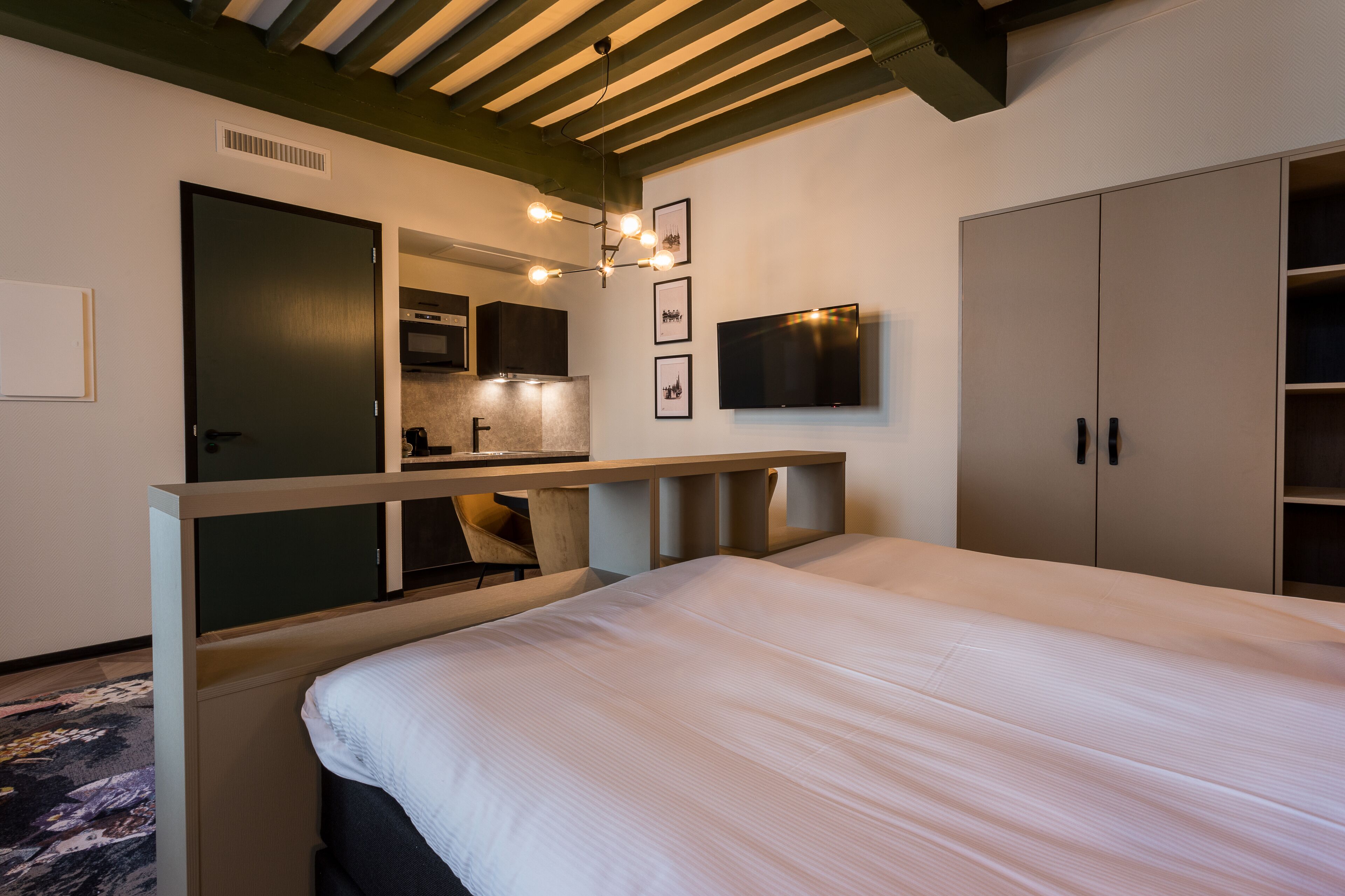 Una habitación de hotel con una cama, televisión montada en la pared, kitchenette y armario.