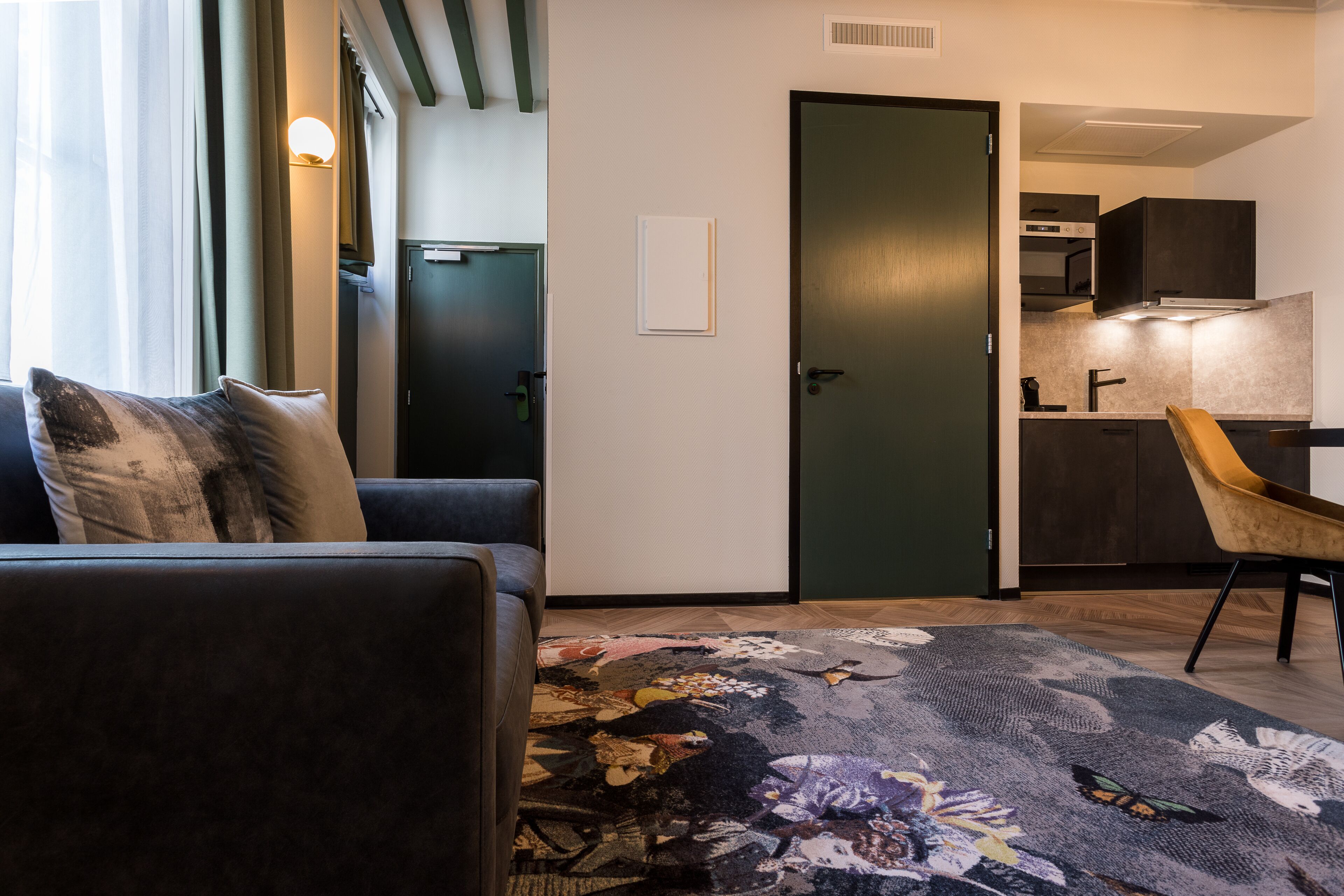 A modern living room with a sofa, a patterned rug, and a door leading to a kitchen area.