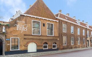 A historic building with a sign reading "HOTEL Rijks". It features large windows, a prominent arched entrance, and a tiled roof.