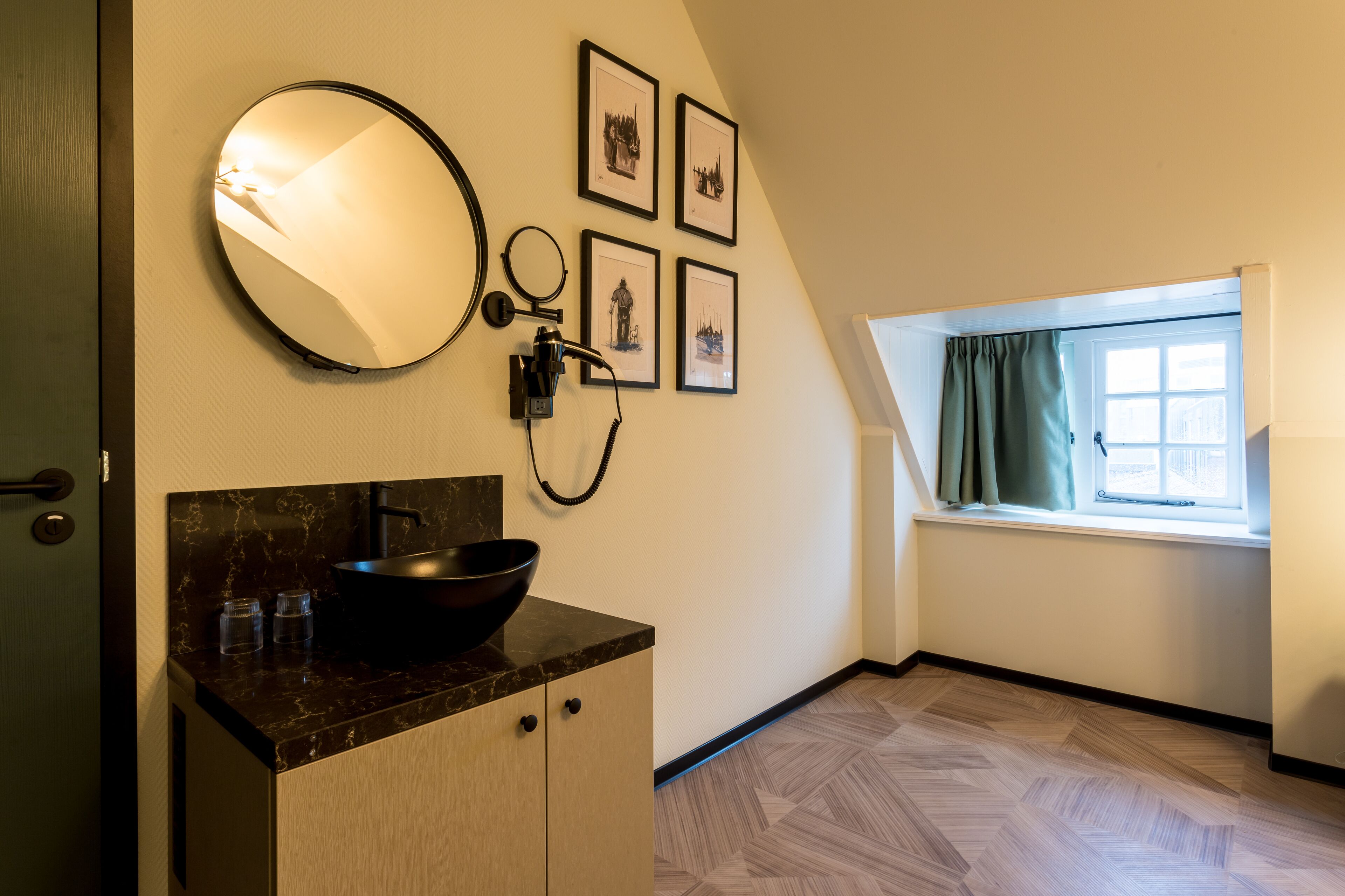 Een badkamer met een zwarte wastafel, een spiegel en vier ingelijste foto’s aan de muur.