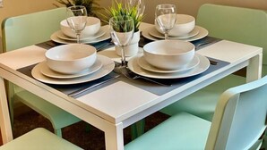 Una mesa de comedor con platos, tazones y copas de vino blancos, rodeada de sillas verdes.