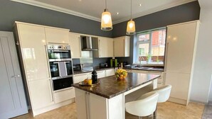 A modern kitchen with white cabinets, stainless steel appliances, a central island with bar stools, and pendant lighting. - Beautiful 4 Bedroom house -5 min walk to the beach (Bournemouth)