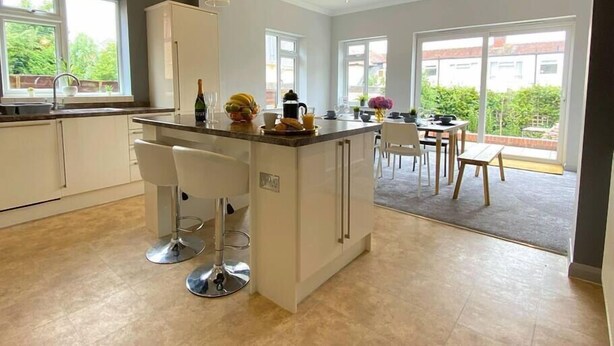 A modern kitchen with a central island, bar stools, and a dining area with a table and chairs. - Beautiful 4 Bedroom house -5 min walk to the beach (Bournemouth)