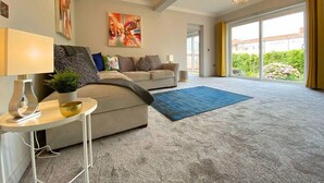 A spacious living room with a large sofa, a coffee table, and a blue rug. There is a chandelier hanging from the ceiling and a painting on the wall. - Beautiful 4 Bedroom house -5 min walk to the beach (Bournemouth)