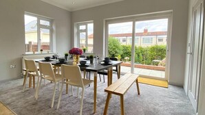 A dining area with a table set for four, chairs, a bench, and a view of the outside. - Beautiful 4 Bedroom house -5 min walk to the beach (Bournemouth)