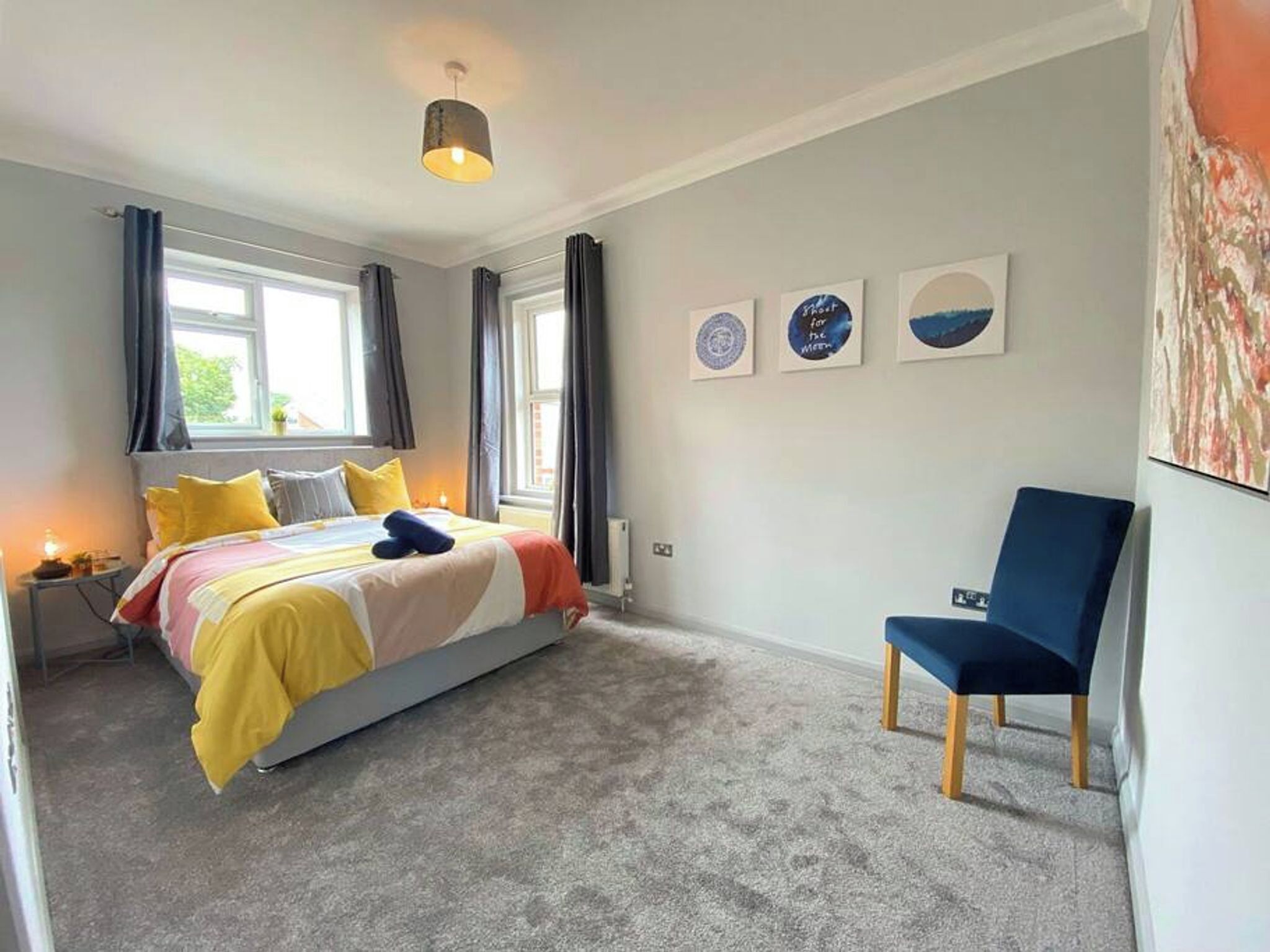 Une chambre à coucher avec un lit, une chaise, une fenêtre et des œuvres d’art accrochées au mur.