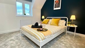 Un dormitorio moderno con una estructura de cama de metal blanco, un edredón a rayas y dos lámparas de noche.
