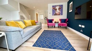 Un salón moderno con un sofá gris, cojines amarillos, un tapete azul estampado y dos sillones rosas.
