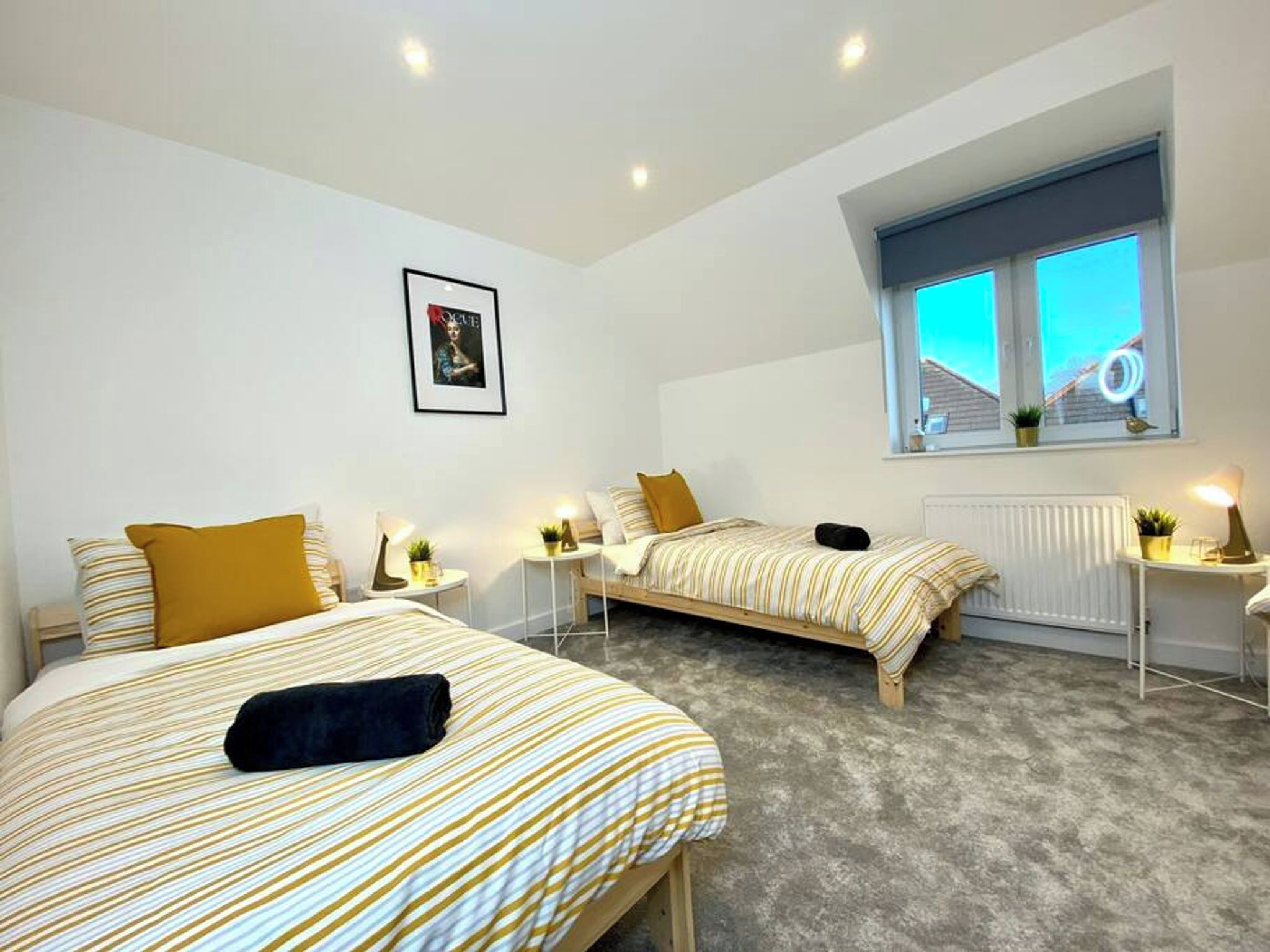 A bedroom with two beds, a window with a view, a radiator, and a framed picture on the wall.