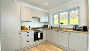 A modern kitchen with white cabinets, a wooden countertop, a built-in oven, and a window with a view of a yellow building.
