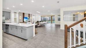 Una cocina moderna con armarios grises, una isla central y un comedor con vistas a la piscina.