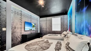 Un dormitorio con una cama grande, un televisor y una pared con un mural de temática espacial.