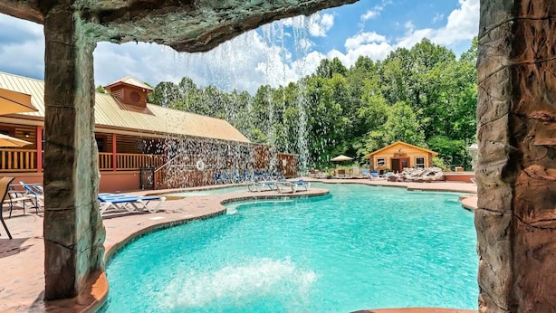 A swimming pool with a waterfall feature, surrounded by lounge chairs and a wooden building. - Super Views, Flat roads, Hot Tub (Gatlinburg)