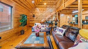 A wooden cabin interior with a staircase, leather sofa, and a dining area. - Super Views, Flat roads, Hot Tub (Gatlinburg)