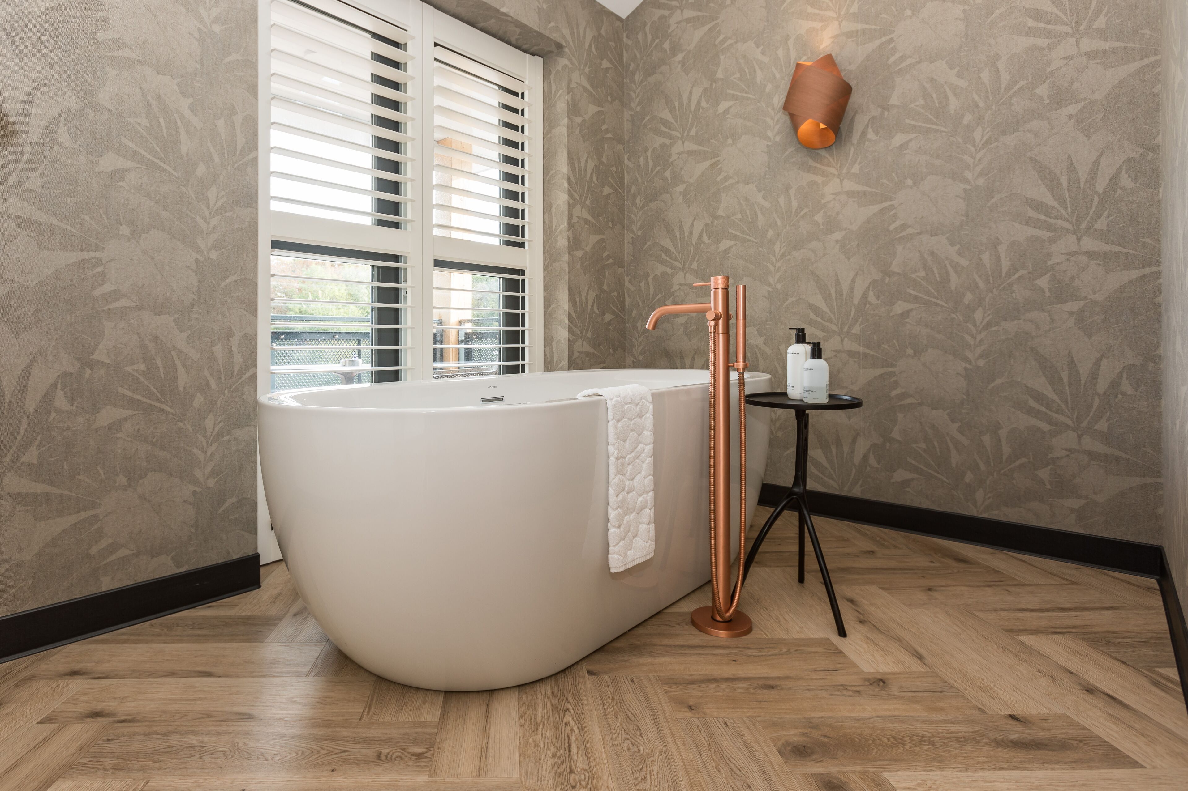 A modern bathroom with a freestanding bathtub, a copper faucet, and a small table with toiletries.