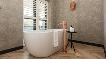 A modern bathroom with a freestanding bathtub, a copper faucet, and a small table with toiletries.
