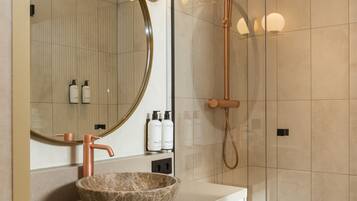 A modern bathroom with a round mirror, a copper faucet, a glass-enclosed shower, and a marble sink.