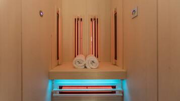 Una sauna con dos toallas sobre un banco, una luz azul en la parte inferior y un panel de control en la pared.