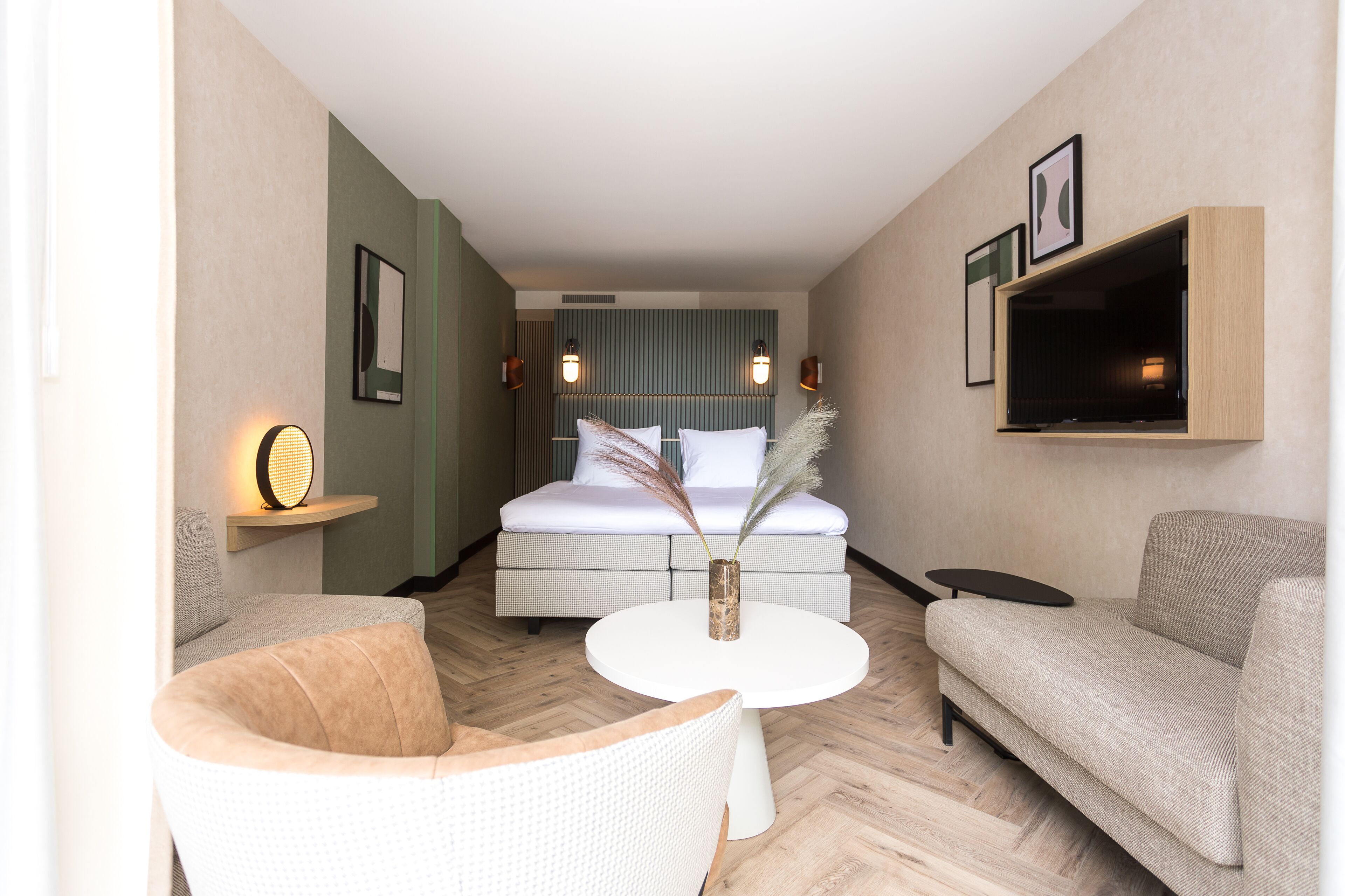 Une chambre d’hôtel avec un lit, deux canapés, une petite table et un téléviseur fixé au mur.