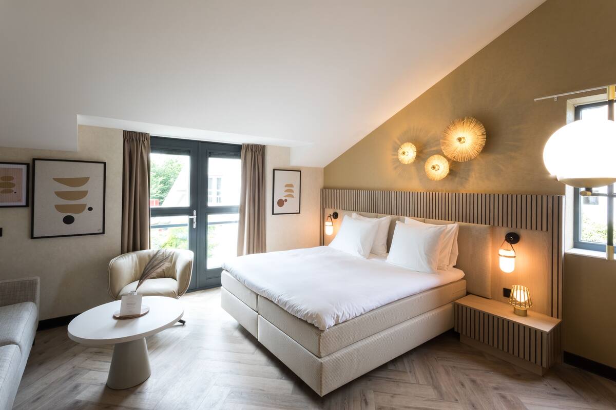 Een moderne hotelkamer met een groot bed, een klein tafeltje, een stoel en een nachtkastje met een lamp.