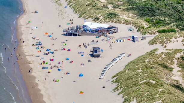 An aerial view of a beach with a large building, beach umbrellas, and people.