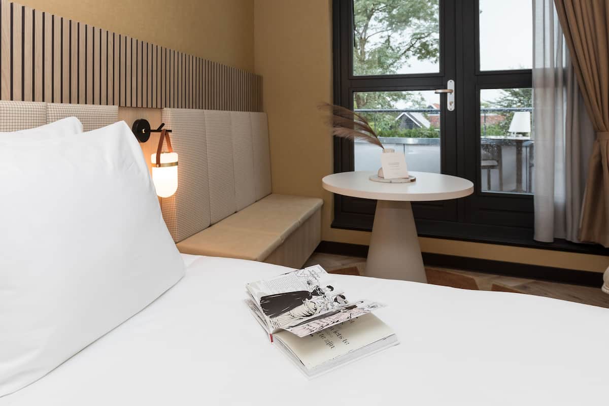 Een hotelkamer met een bed, een klein tafeltje met een kaars en een raam met gordijnen.