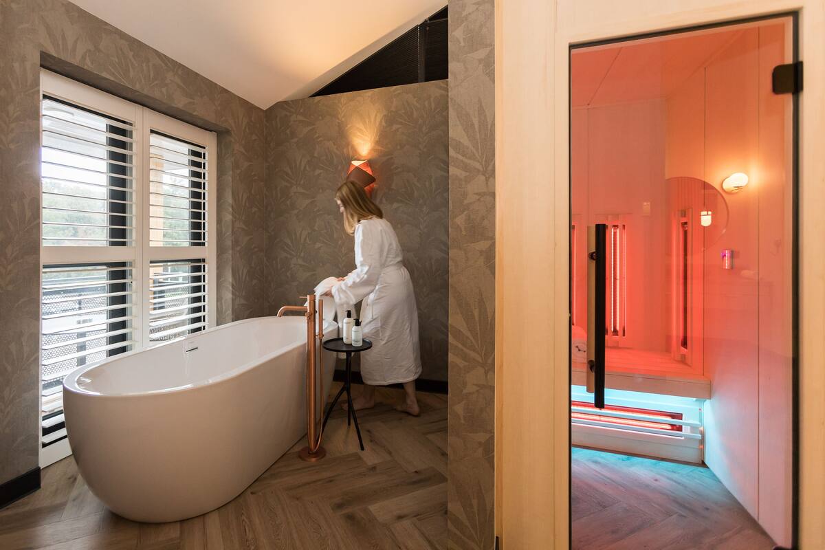 Een moderne badkamer met een vrijstaand bad, een wastafel met spiegel en een wandlamp.