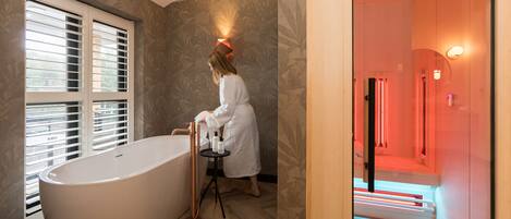 A modern bathroom with a freestanding bathtub, a vanity with a mirror, and a wall-mounted light fixture.