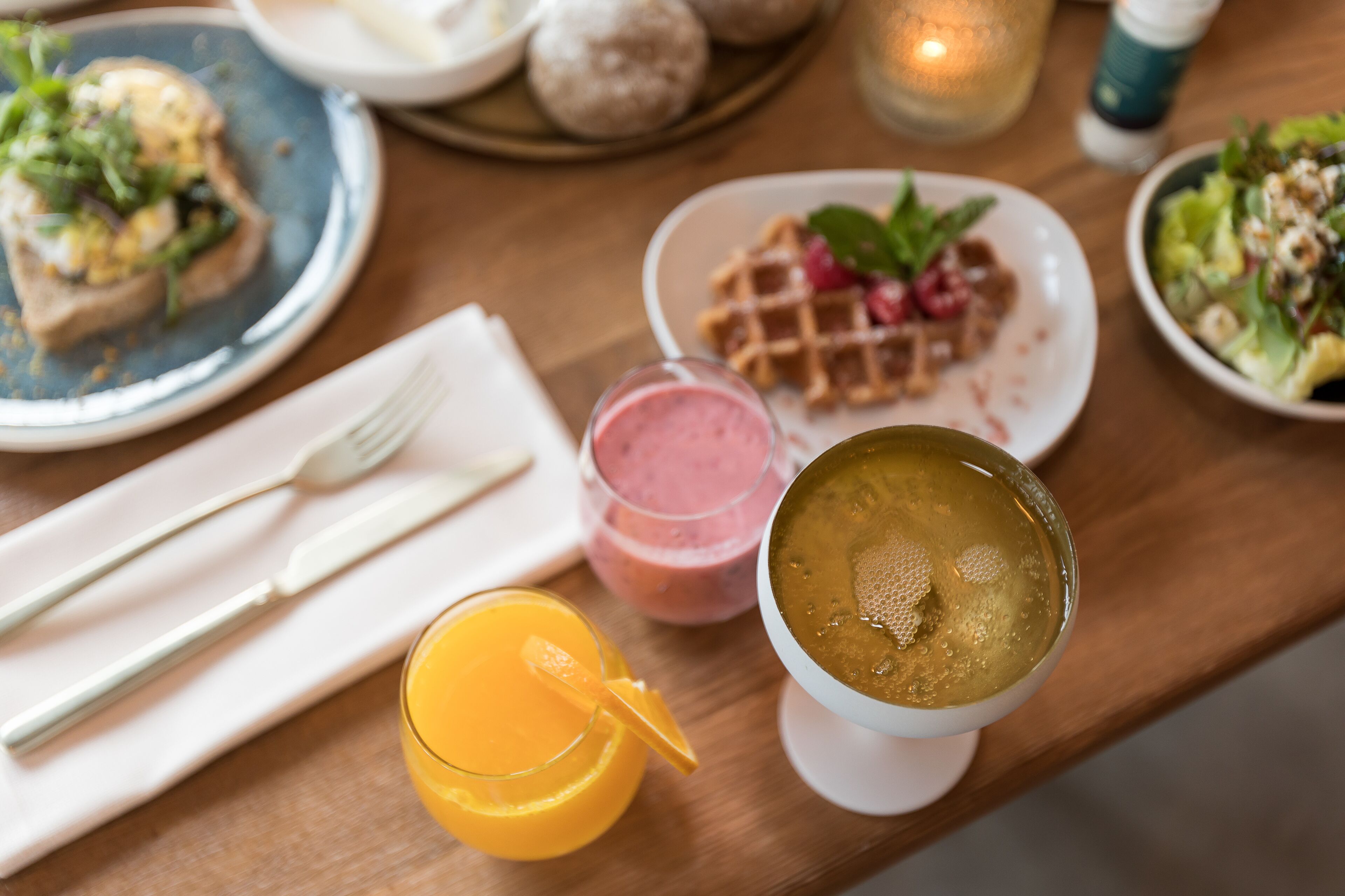 Une table de petit-déjeuner avec divers plats, notamment des gaufres, un smoothie et un bol de soupe.