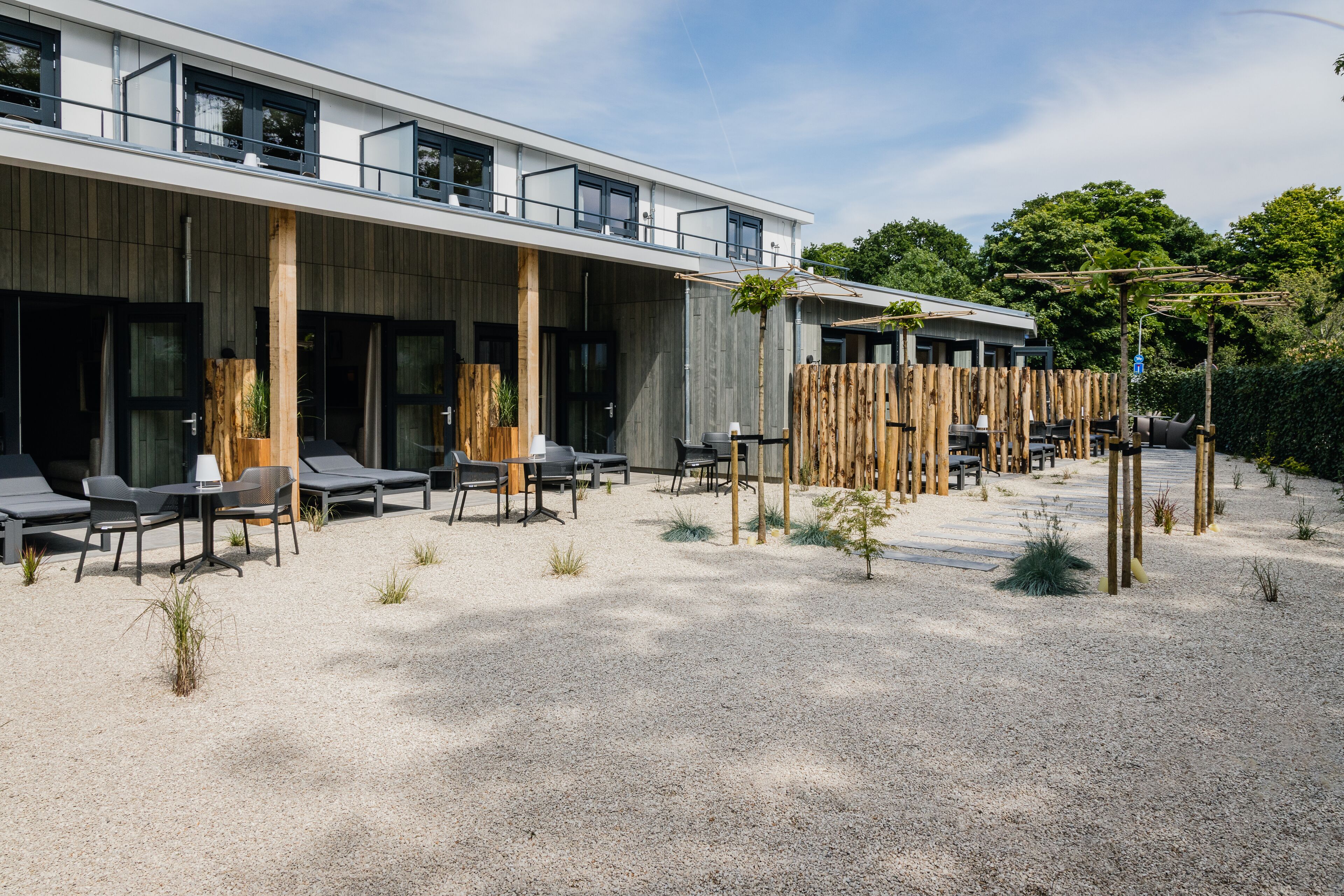 A modern building with a covered outdoor seating area, a gravel ground, and a wooden fence.