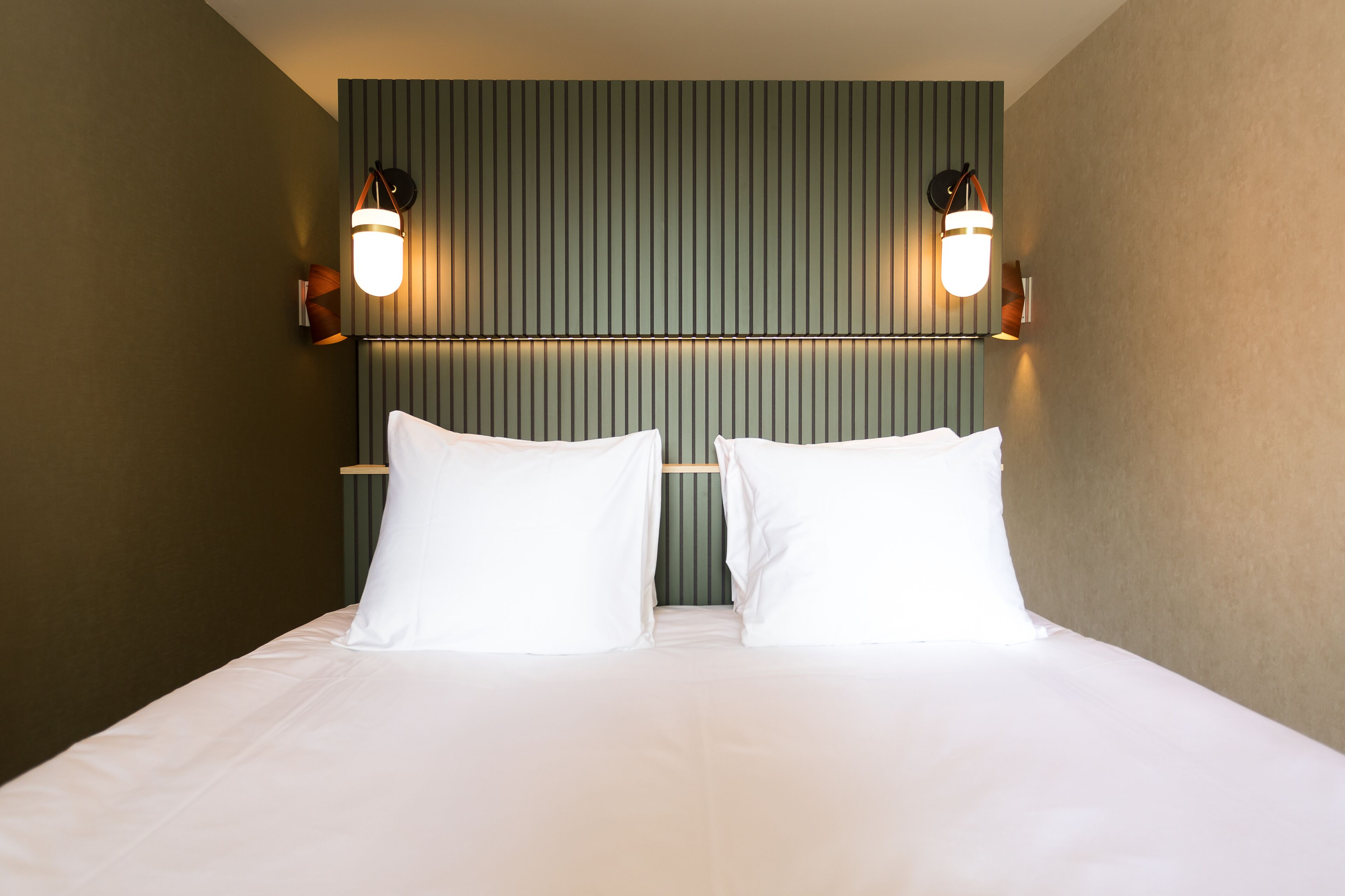 A hotel room with a bed, two wall-mounted lights, and a striped headboard.
