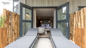 A modern outdoor lounge area with two reclining chairs, a small table, and a wooden fence.
