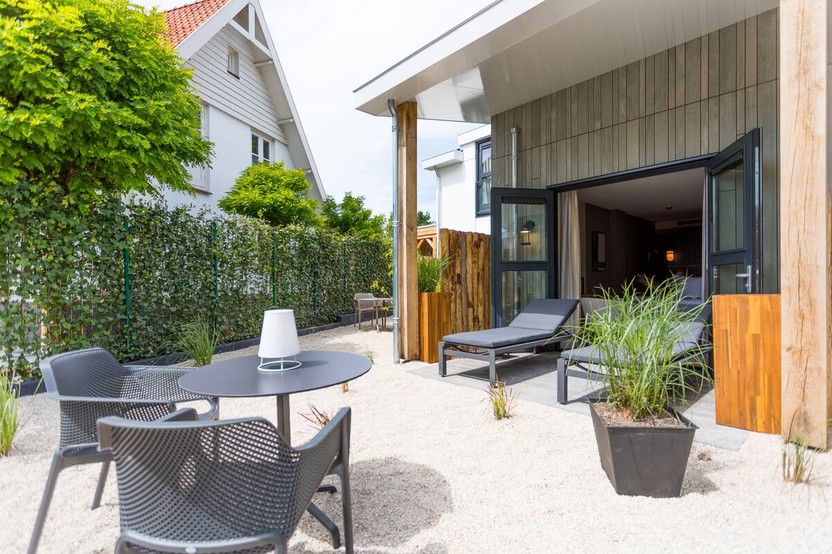 Een terras buiten met een tafel, stoelen, een potplant en een houten omheining.