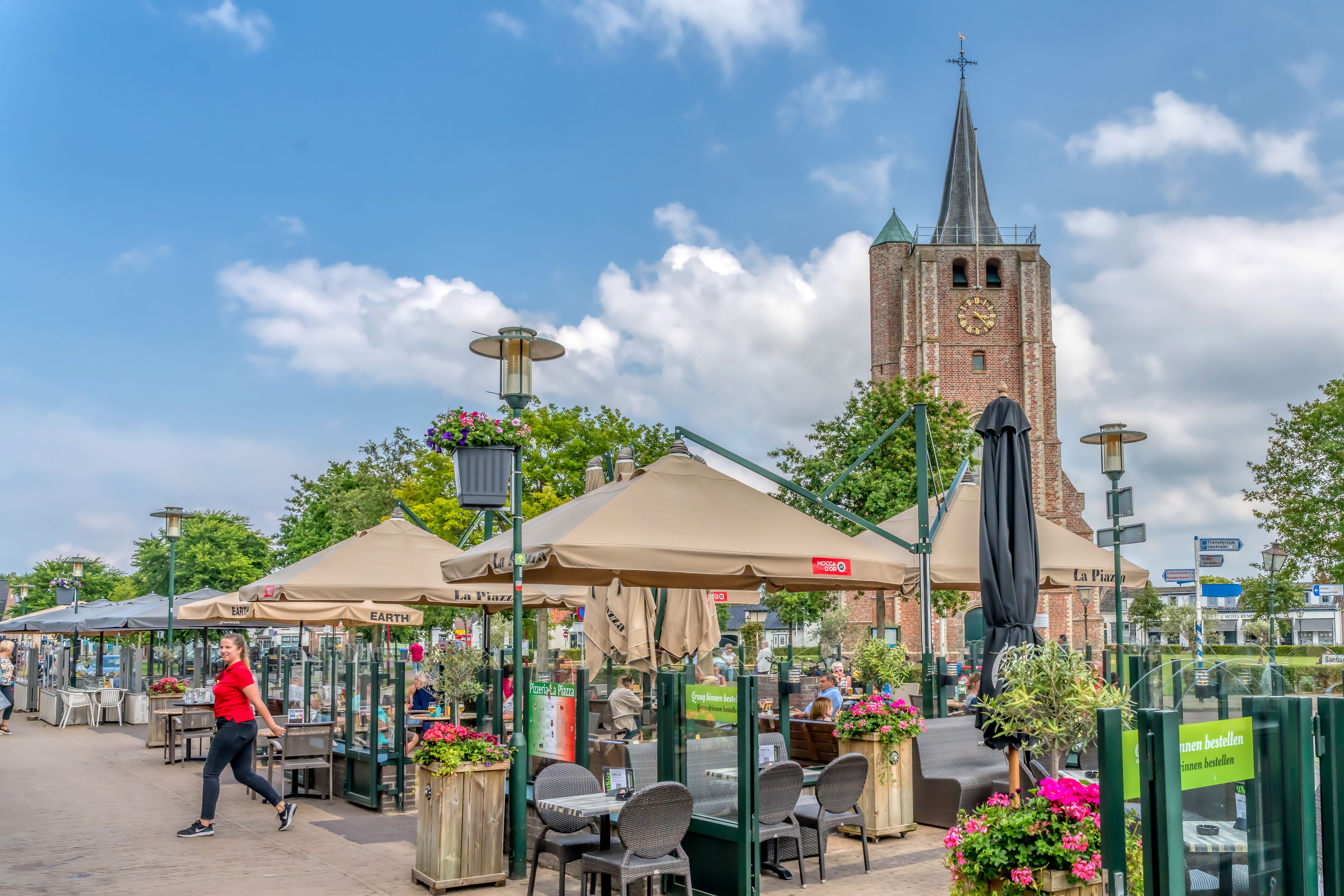 Sitzgelegenheiten im Freien mit Sonnenschirmen, ein Ziegelturm und klarer Himmel.