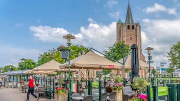 Sitzgelegenheiten im Freien mit Sonnenschirmen, ein Ziegelturm und klarer Himmel.