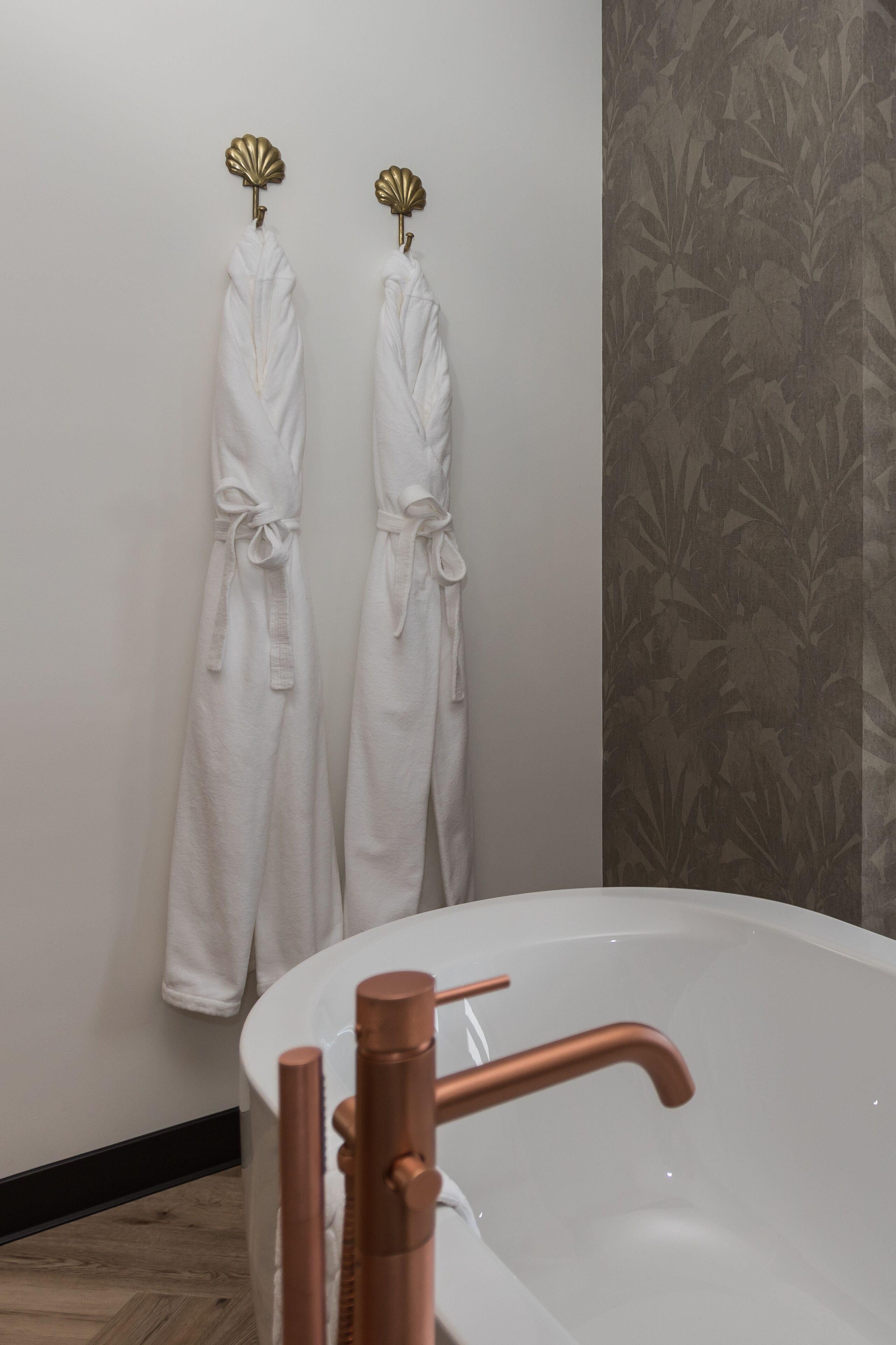 A bathroom with a bathtub, two towels hanging on hooks, and a patterned wallpaper.