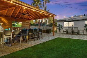 An outdoor patio with a covered seating area, a TV screen, and a pool table. - Backyard Paradise w/ Hot Tub & Heated Pool ! (Scottsdale)