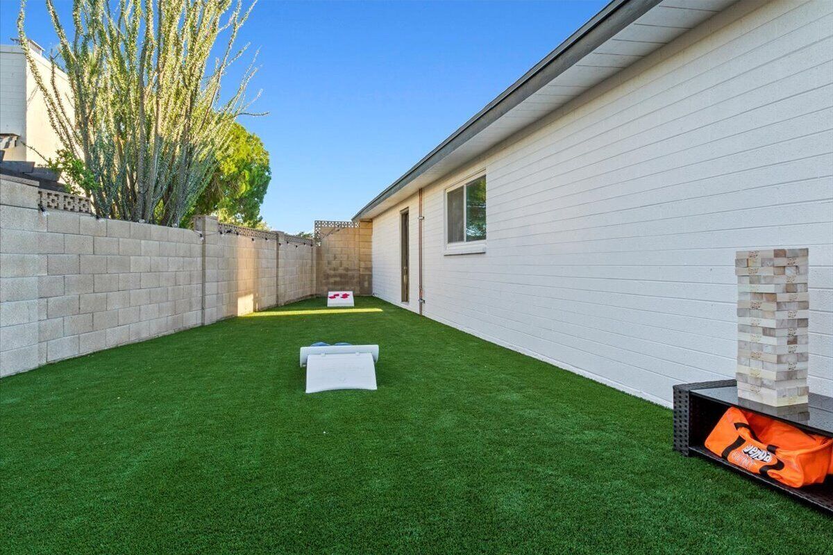 A backyard with artificial grass, a brick wall, and a white building.
