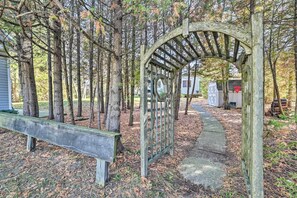Step through the rustic archway into a serene natural setting surrounded by tall trees and a well-maintained pathway.