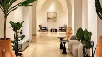 A modern interior with arched ceilings, a central seating area with sofas and tables, and large potted plants.