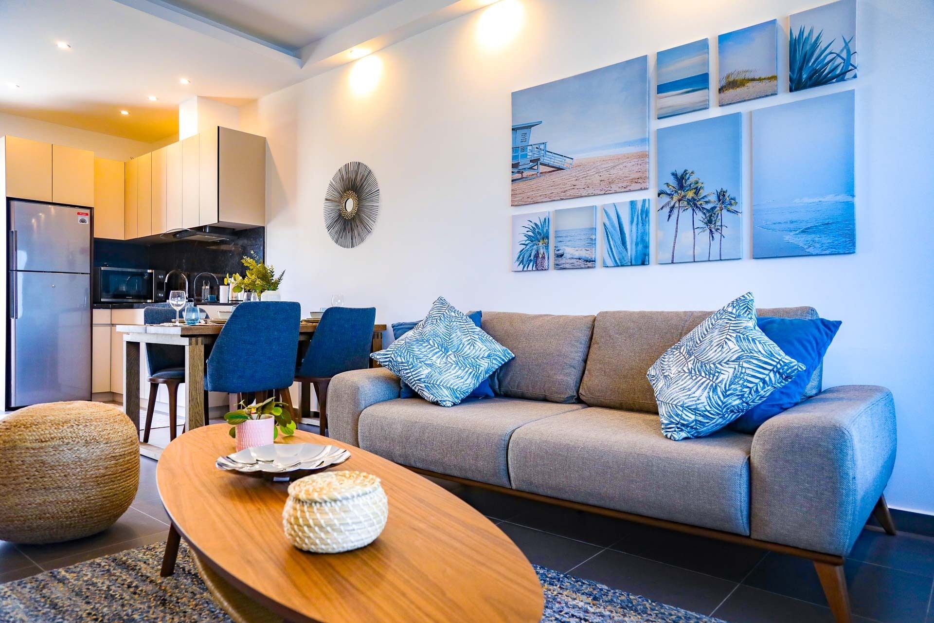 A modern living room with a grey sofa, blue cushions, a wooden coffee table, and a kitchen in the background.