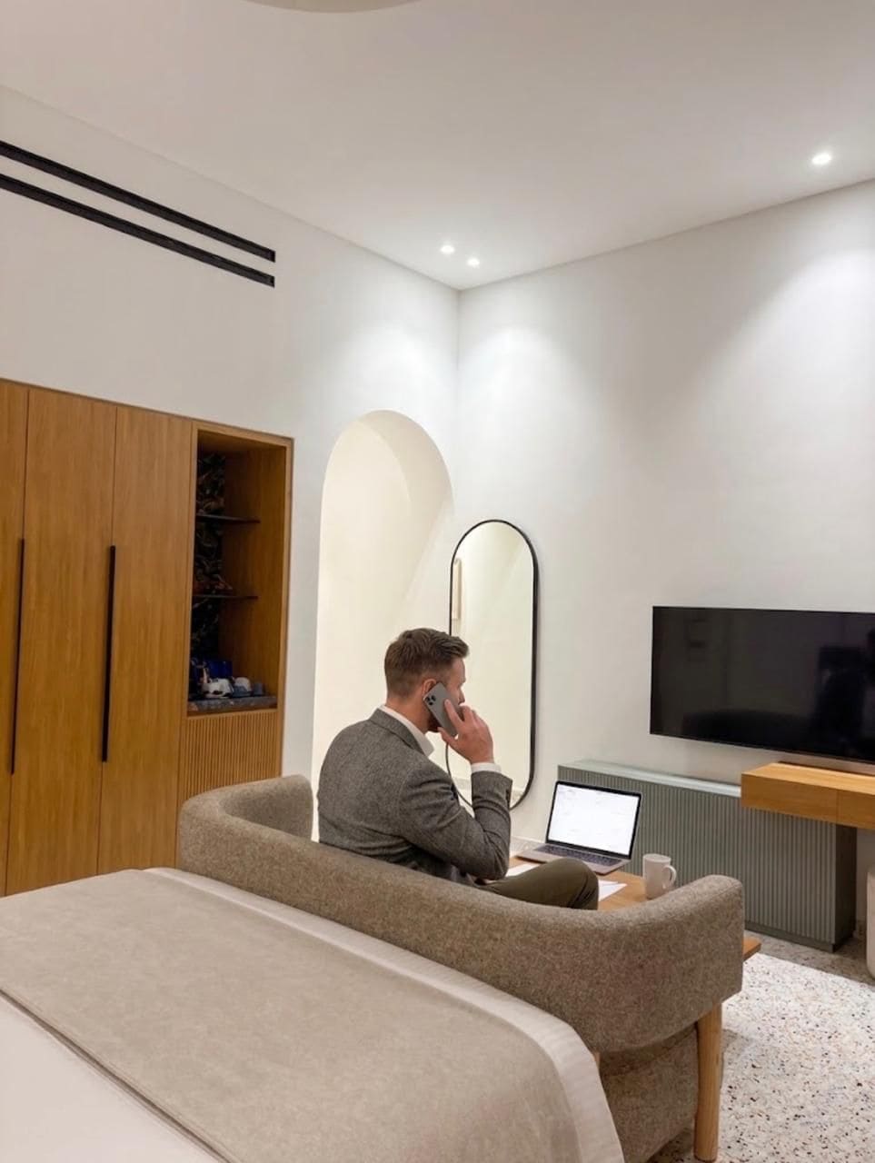 A modern hotel room with a bed, a desk with a laptop, a TV, and a wardrobe.