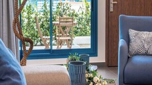 A modern room with a sofa, a lamp, a table with flowers, and a view of an outdoor area with a wooden structure. - The Lead Hotel (Freetown)