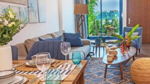Un salon moderne avec un canapé, une table basse et une table à manger, cette dernière étant dressée avec des assiettes, des verres et un vase de fleurs.