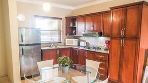 A kitchen with wooden cabinets, a stainless steel refrigerator, a microwave, a gas stove, and a glass dining table with chairs. - Beautiful Studio in Ocean Dream Cabarete (Cabarete)