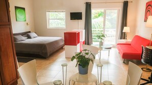 A modern hotel room with a bed, a red sofa, a glass dining table with chairs, a TV, and a potted plant. - Beautiful Studio in Ocean Dream Cabarete (Cabarete)