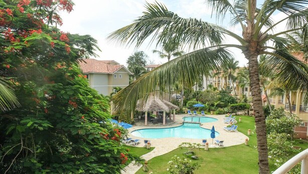 A pool area with lounge chairs and a thatched-roof pavilion, surrounded by palm trees and greenery. - Beautiful Studio in Ocean Dream Cabarete (Cabarete)