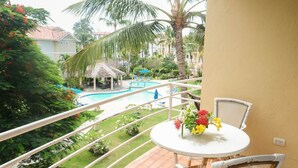 A balcony with a view of a swimming pool, palm trees, and a thatched-roof structure. - Beautiful Studio in Ocean Dream Cabarete (Cabarete)